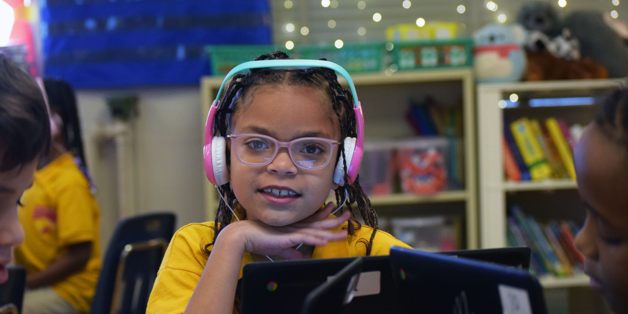 Student in pink headphones and glasses working on a laptop.