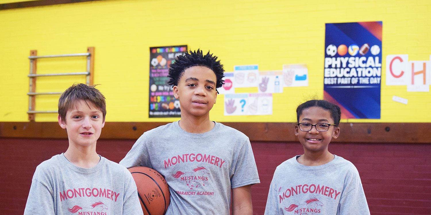 Three Montgomery Mustangs students in the gym, one holding a basketball.